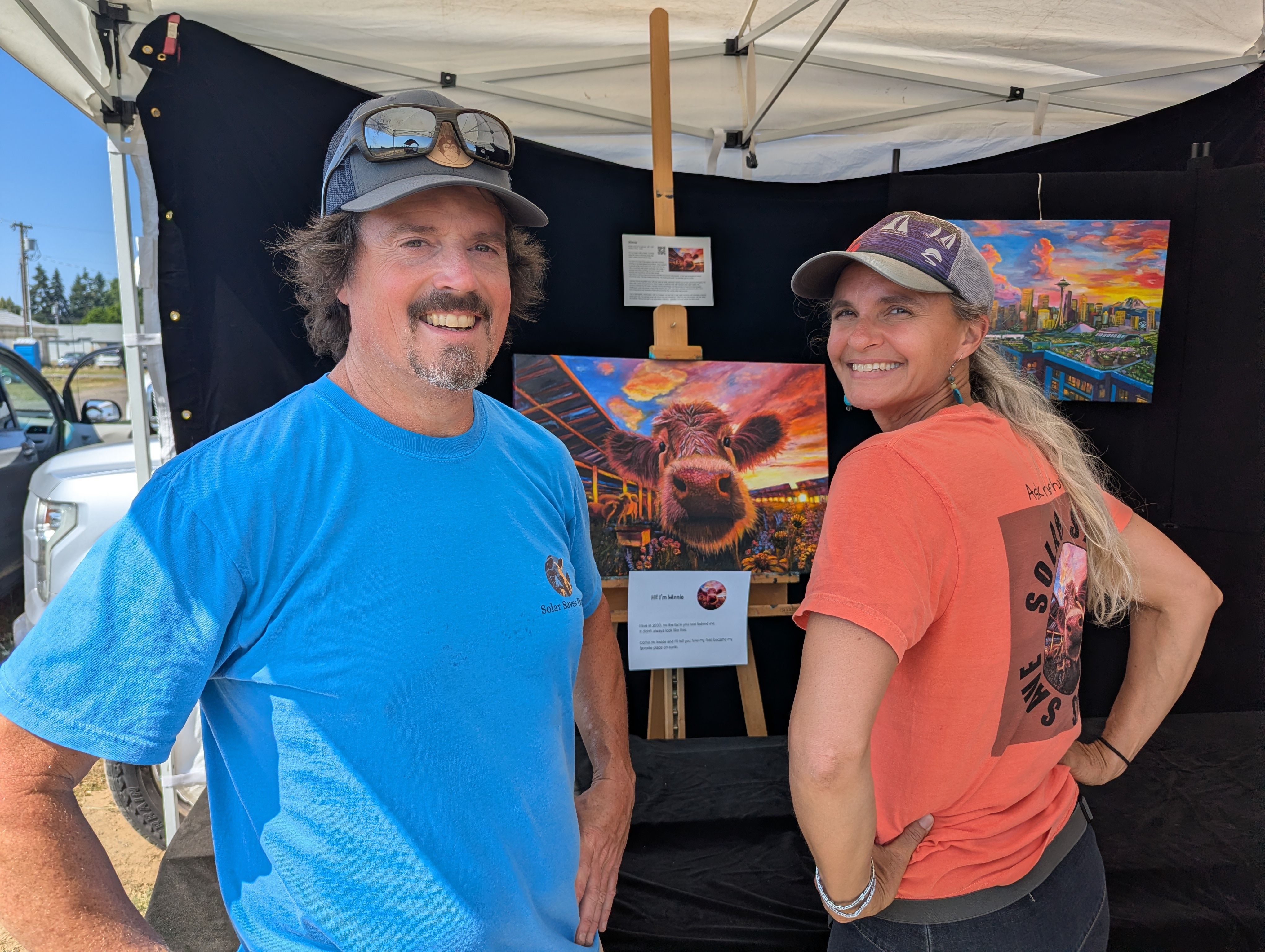 Two people smiling at a field day booth beside the Winnie painting